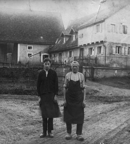 Friedrich Ortner senjor und Friedrich Ortner junior im Jahr 1938 auf einer Schwarzweißfotografie vor dem ca. 300 Jahre alten Wohnhaus mit Schreinerei.