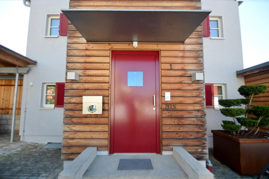 Rote Haustüre mit Überdachung, eingerahmt mit warmen Quer-Holz-Leisten
